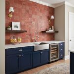 Blue kitchen cabinets with a white farmhouse sink and a wine cooler, complemented by a red textured tile backsplash and moder.