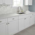 Bright white kitchen featuring a shell tile backsplash, sleek countertop, and contemporary fixtures for a clean, stylish look.