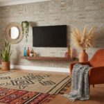A close-up of beige stone tiles with textured surface in a living room setting, complemented by a wall-mounted TV, plants, an.