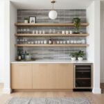A modern kitchen featuring a glass tile backsplash, wooden shelves, and a mini wine fridge, creating a sleek and functional s.