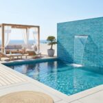 Outdoor pool featuring a striking blue glass tile backsplash and waterfall feature, perfect for relaxing by the sea.