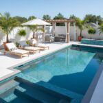Luxurious outdoor pool area featuring glass tile backsplash and mosaic details, surrounded by tropical plants and comfortable.