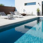 A modern outdoor pool area featuring glass mosaic tiles, sleek white furniture, and minimalist design elements.