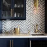 Modern kitchen backsplash with peel and stick tile in a herringbone pattern, featuring gold accents and navy cabinetry.