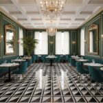 Elegant dining room featuring green walls, gold accents, and a black-and-white geometric tiled floor. Crystal chandeliers and.
