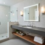 A modern bathroom featuring a shell tile wall and a sleek vanity with a large mirror, illuminated by wall sconces, showcasing.