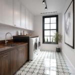 Bright laundry room with white and gray patterned ceramic tiles, wooden cabinetry, and a large window for natural light.