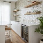 A modern kitchen featuring a beautiful mother of pearl shell tile backsplash with floating wooden shelves and a white counter.