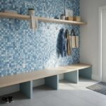 Interior view of a modern entryway with a blue mother of pearl shell tile wall and a wooden bench.