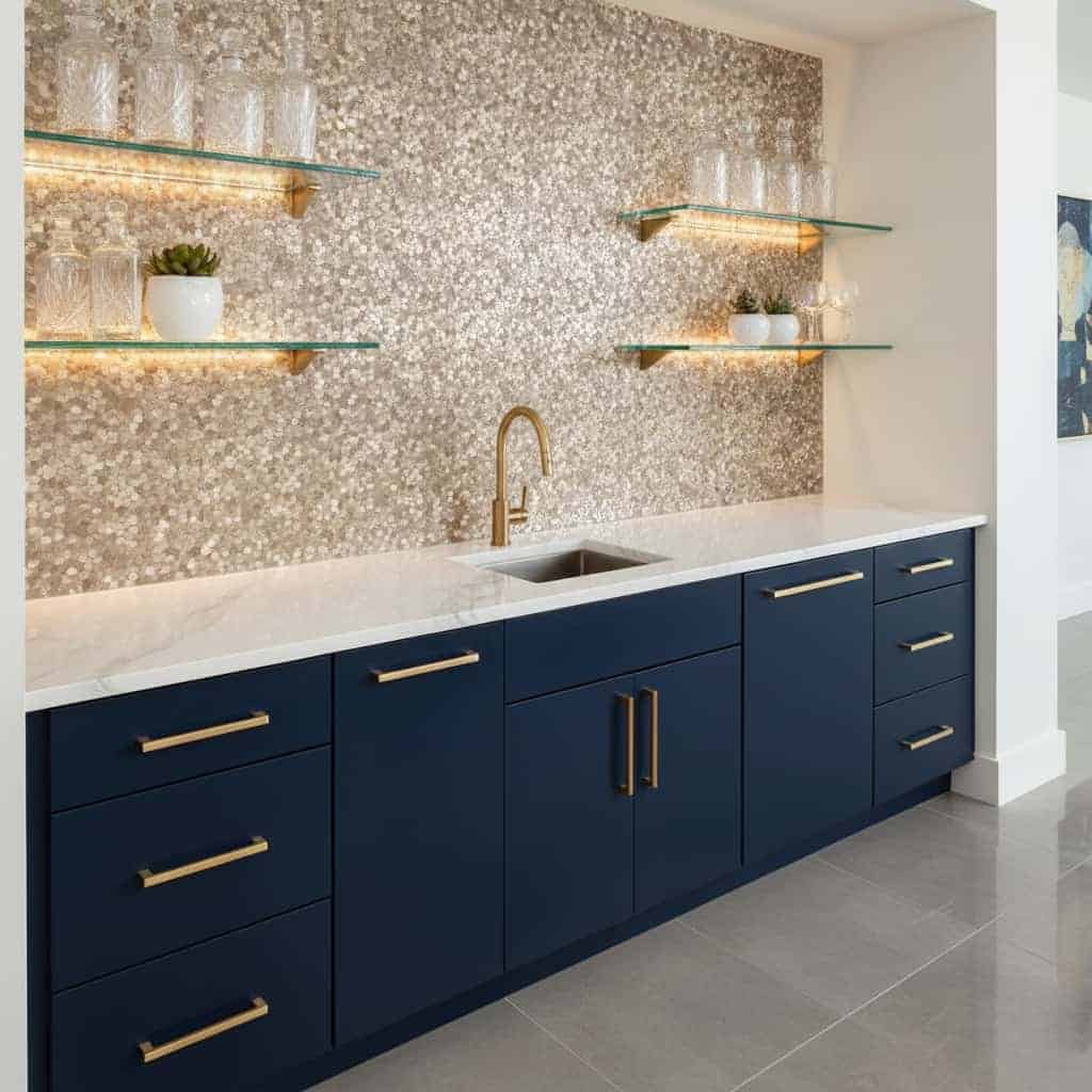 A modern kitchen featuring peel and stick tile backsplash with a sleek navy blue cabinet and gold hardware.