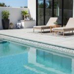 Modern outdoor pool area featuring glass mosaic tile along the pool edge and contemporary lounge chairs.