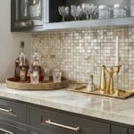 Up of a kitchen countertop featuring a mother of pearl shell tile backsplash, with glassware and gold accents creating a luxu.
