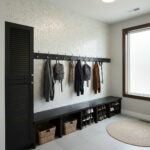 A modern entryway with a shell tile accent wall, hooks for coats, and a black storage bench with baskets, featuring seashell-.