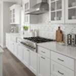 A modern kitchen featuring a stunning mother of pearl shell tile backsplash with white cabinetry and stainless steel applianc.
