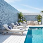 Poolside area with glass mosaic tile backsplash, lounge chairs, and outdoor seating with plants.