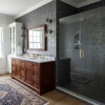 Dark gray mosaic tile with textured surface in shower area, complementing wooden vanity and classic decor.