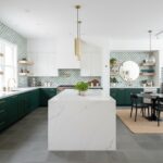 Bright kitchen featuring green lower cabinets, white upper cabinets, and a marble island. Decor includes open shelves, round.