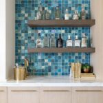 A stylish glass tile backsplash with two wooden shelves holding bottles and decor, enhancing kitchen or bar area aesthetics.