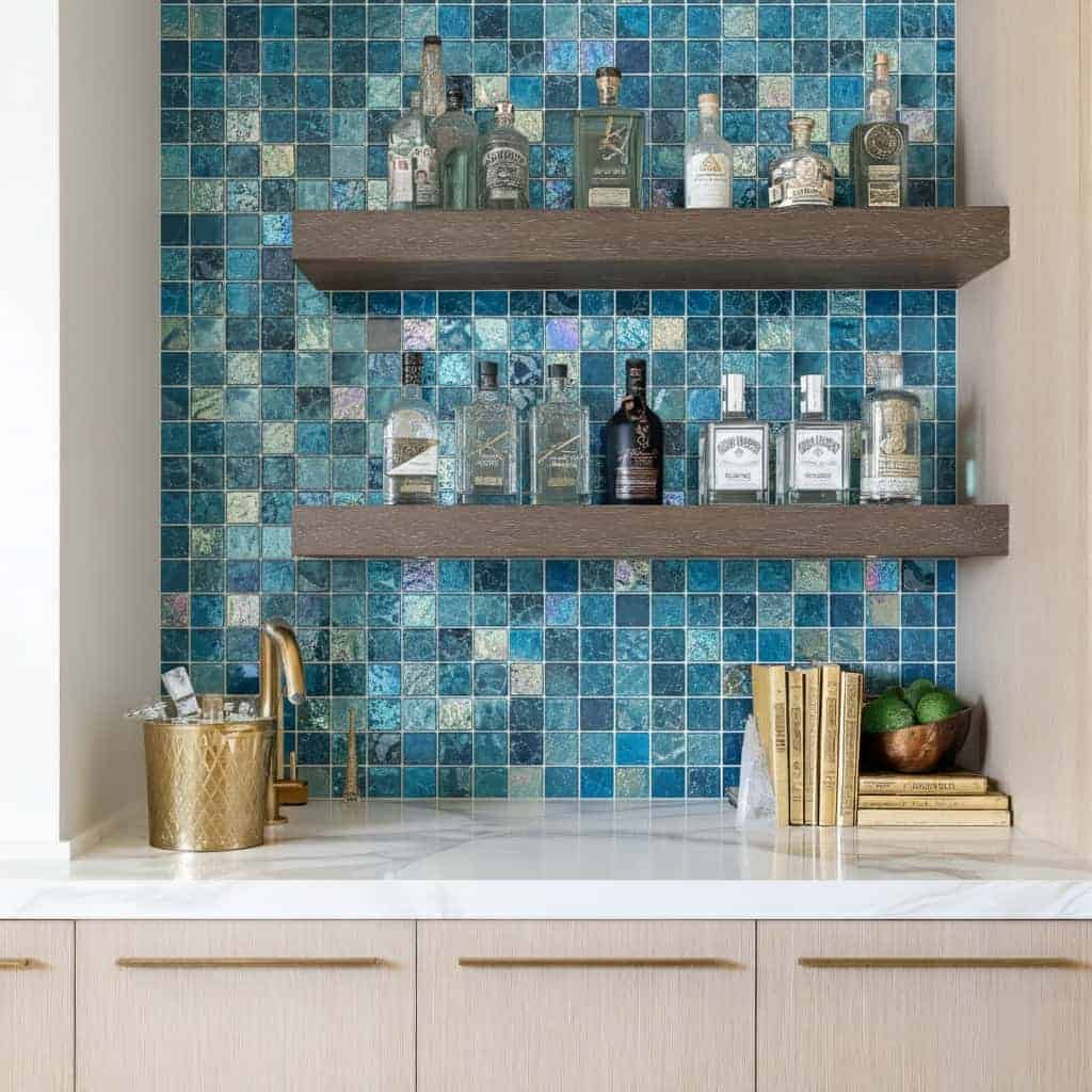 A stylish glass tile backsplash with two wooden shelves holding bottles and decor, enhancing kitchen or bar area aesthetics.
