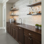 Mother of pearl shell tile backsplash in a modern kitchen with dark wood cabinetry and floating shelves.