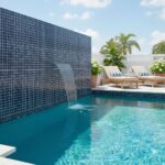A stunning outdoor pool with a glass tile backsplash, featuring a waterfall feature and lounge area with tropical plants for.