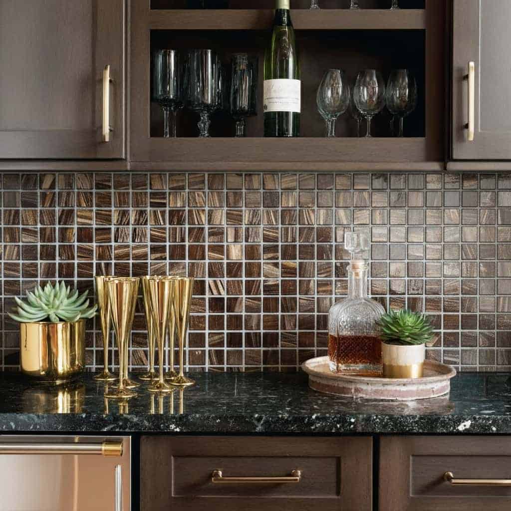 Decorative glass tile backsplash in a contemporary kitchen with glassware and plants.