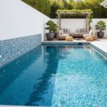 A modern outdoor pool area featuring a blue glass mosaic tile backsplash along the pool edge, complemented by stylish outdoor.