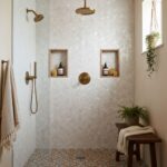 Elegant bathroom shower wall featuring mother of pearl shell tiles with built-in niches and brass fixtures.