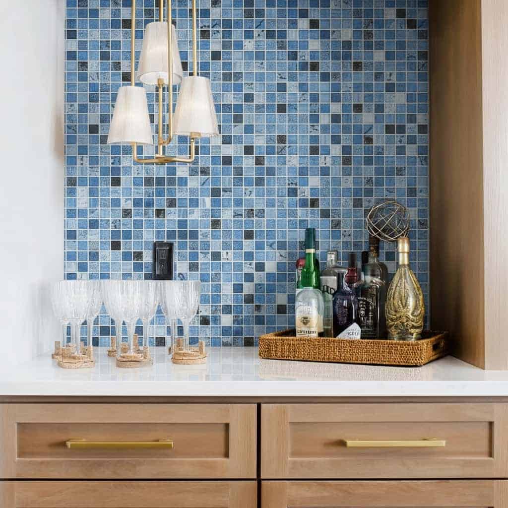 Blue glass tile backsplash with barware and bottles for home decor.