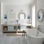 Bright bathroom with white textured tiles, double sinks, and a freestanding bathtub. Features light blue cabinetry, round mir.