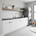 Bright laundry room featuring a sleek shell tile backsplash behind the sink. Modern design with white cabinetry and stacked w.