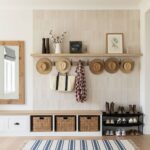 A wall-mounted hat rack with straw hats, a tote bag, and decorative items on a beige tiled wall.