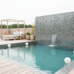 Mosaic tile in shades of gray with textured surface, water feature, and outdoor lounge area with cushions and potted plants.