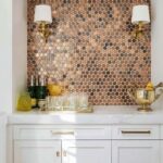Brown mosaic tile wall with textured, round tiles, gold wall sconces, and a white countertop with decorative bottles and a bo.
