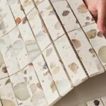 Light beige marble tile with embedded pebble accents, smooth texture, and glossy finish.