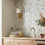 Neutral-toned mosaic tile backsplash with textured surface and small square pattern, complemented by gold fixtures and decora.