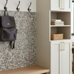 Beige mosaic tile wall with hooks holding bags and scarves, adjacent to a white cabinet and wooden console table with decorat.
