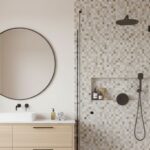 Beige mosaic tile with textured surface in a bathroom, featuring a round mirror, black fixtures, and a minimalist design.