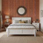 A round mirror with a dark frame hangs above a white bed with neutral pillows, set against a warm wooden paneled wall in a co.