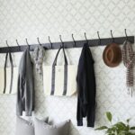 A wall-mounted coat rack with hooks holding bags, hats, and scarves in a modern entryway.