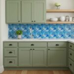 Green kitchen cabinets with black hardware and a blue mosaic tile backsplash.