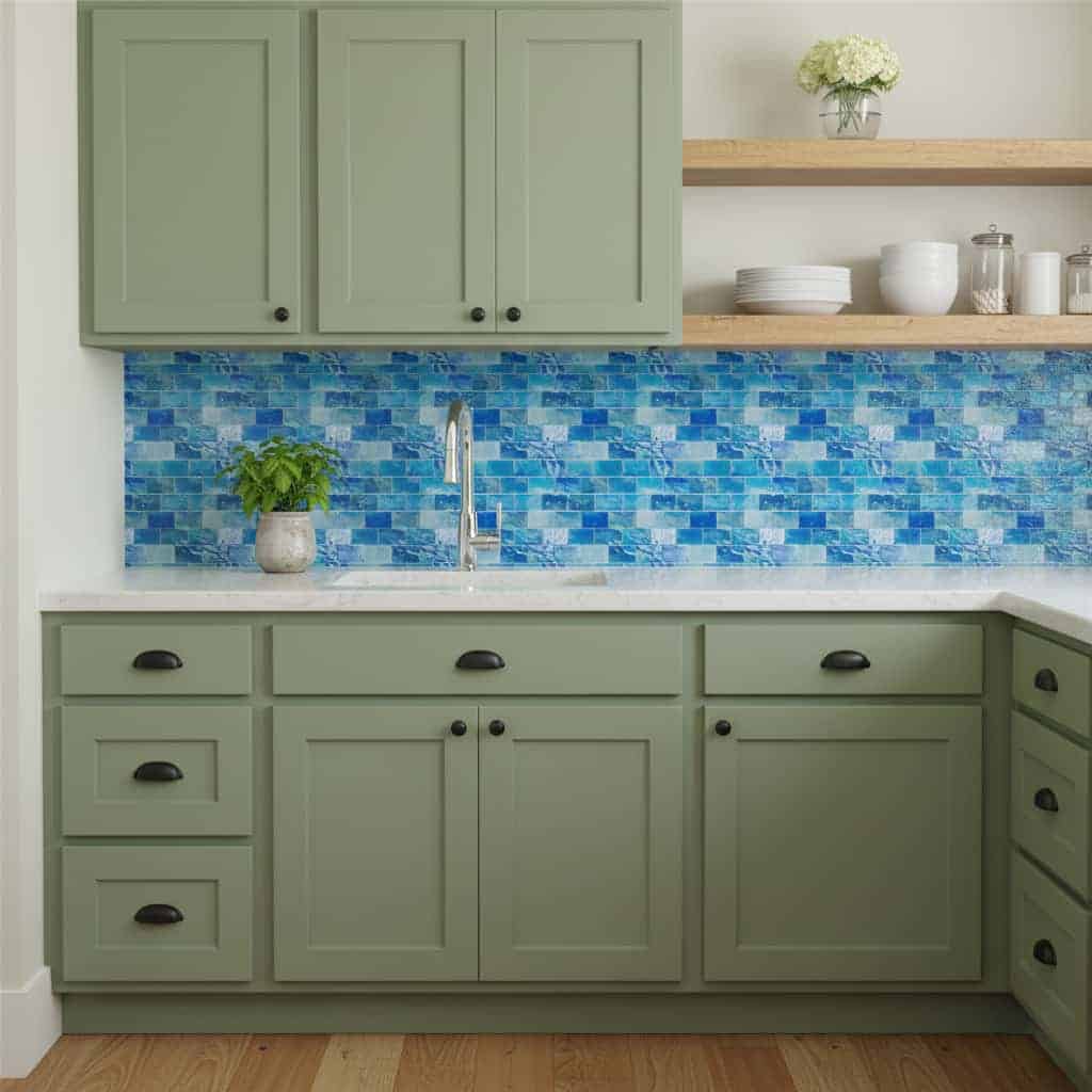 Green kitchen cabinets with black hardware and a blue mosaic tile backsplash.