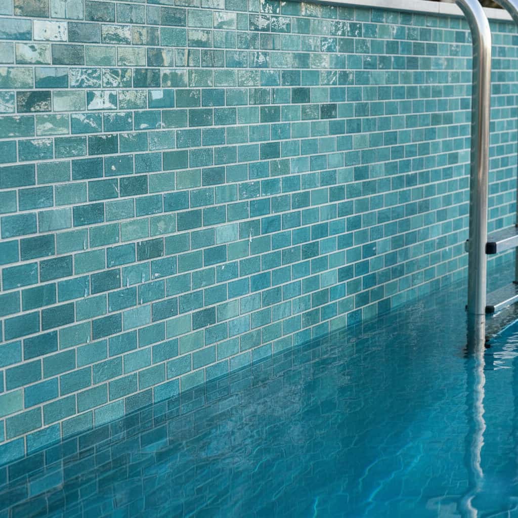 Aqua blue mosaic tiles with glossy texture, arranged in a brick pattern, used on a pool wall.