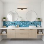 Bright bathroom with round mirrors, white sinks, and a blue mosaic tile backsplash. Features a light wood cabinet and minimal.