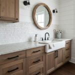 Wooden cabinetry with black handles and a white farmhouse sink with a black faucet, complemented by white subway tile backspl.