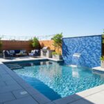Blue mosaic tile wall with water feature, poolside seating, and modern outdoor design.