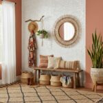 Woven wall mirror, rattan baskets, and textured white tile wall create a warm, inviting entryway. Natural tones and plants ad.