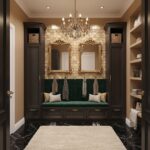 A luxurious entryway with dark wood cabinetry, gold-framed mirrors, and a plush green velvet bench. Features a brick wall, ch.