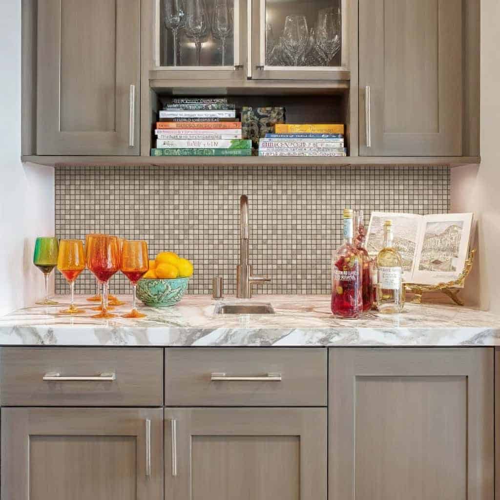 Beige mosaic tiles with smooth texture in a kitchen backsplash, complementing gray cabinetry and marble countertop.