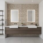 A bathroom with beige stone tiles on the wall, featuring two white sinks, black fixtures, and a floating brown vanity.